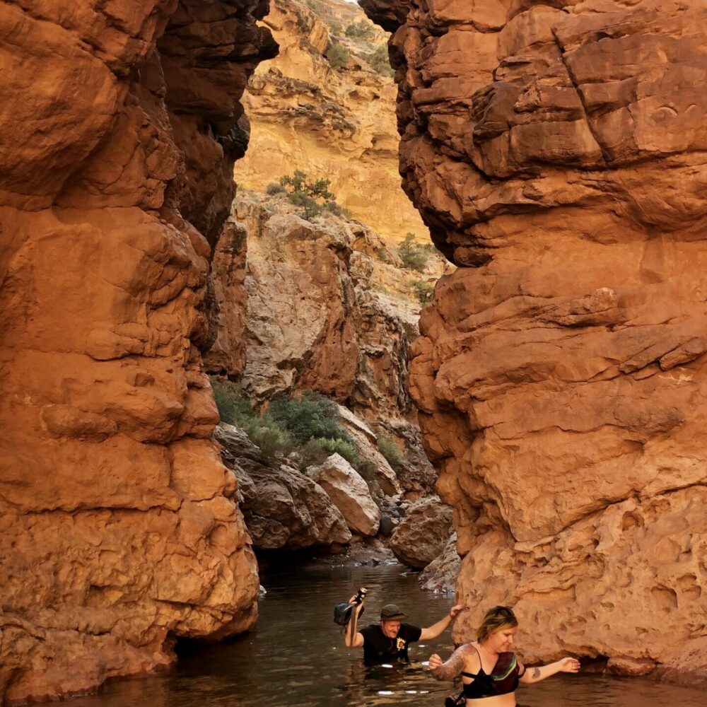 woman and man hiker in water up to their waist wade through slot canyon in capitol reef national park