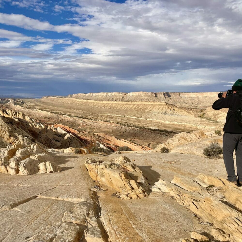 photographer taking photo of the Strike Valley, Waterpocket Fold district, Capitol Reef National Park. He's standing on white sandstone cliffs.